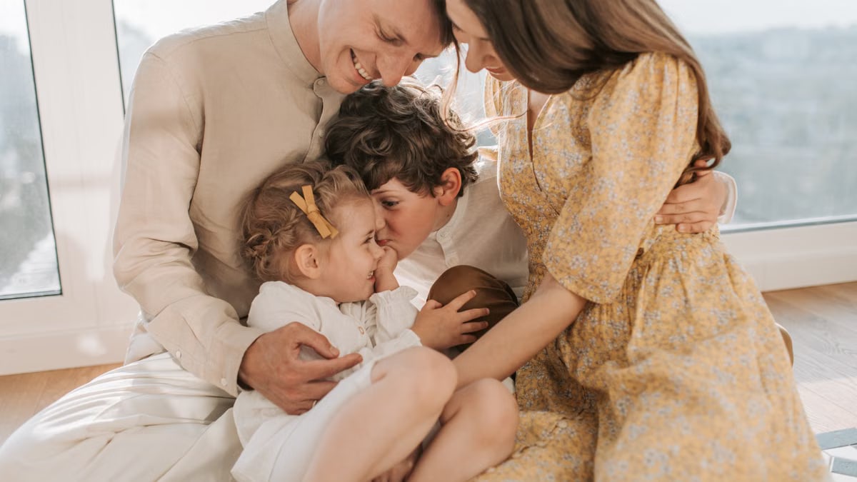 A happy family of four sitting together and sharing a loving moment indoors.